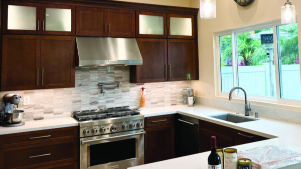 Remodeled kitchen with dark wood tone cabinets, white countertops, and marble backsplash in brown tones