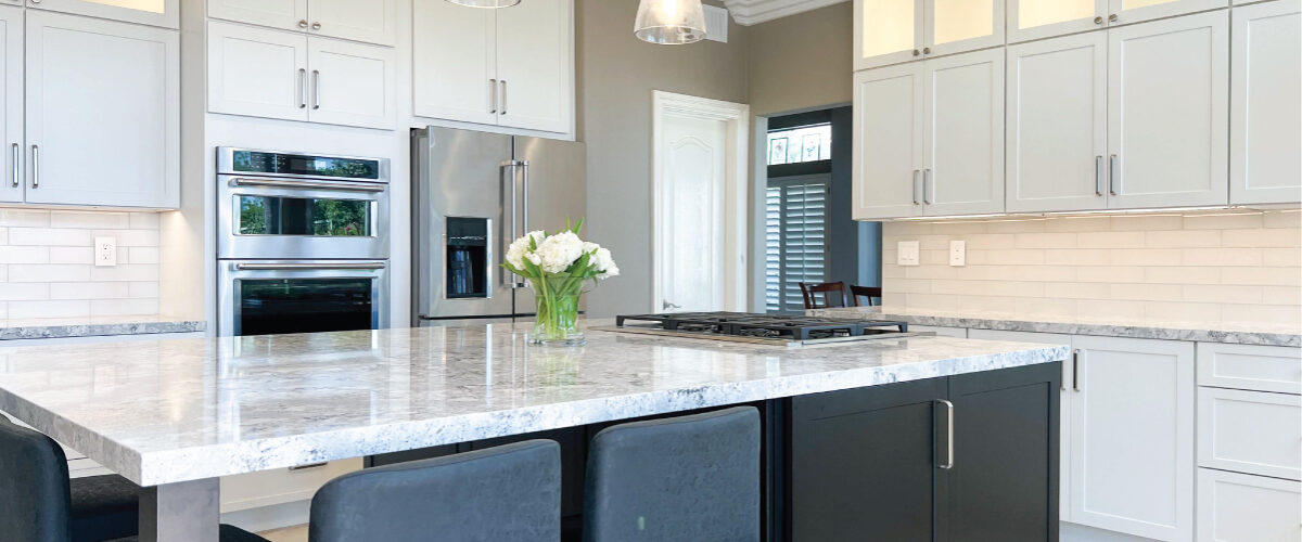 Black kitchen island with seating and white perimeter cabinets with Cambria quartz countertops